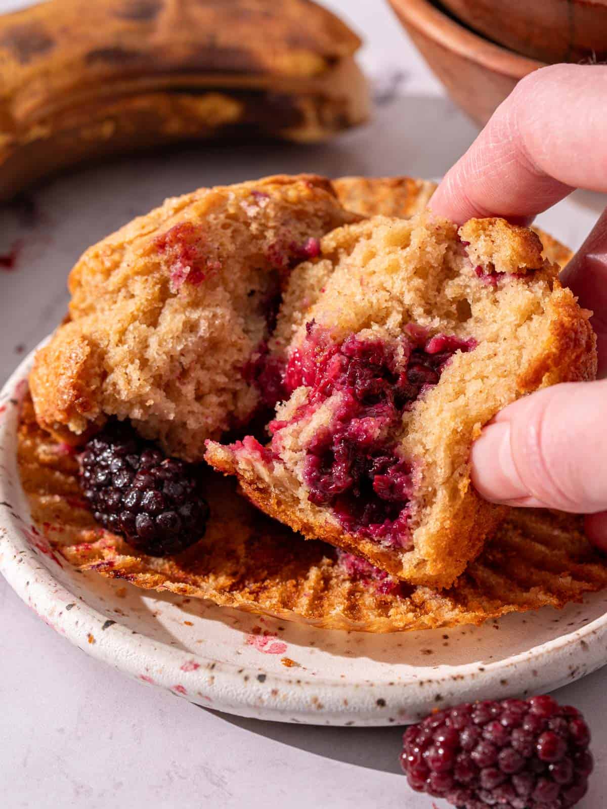 Showing the fluffy and moist banana muffins with juicy blackberries inside.
