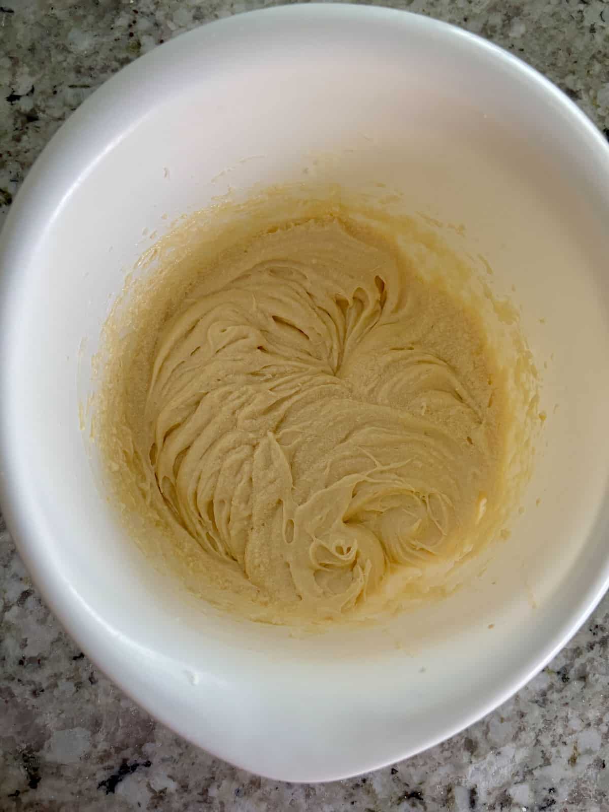 Eggs being added to the butter and sugar mixture in a white bowl.