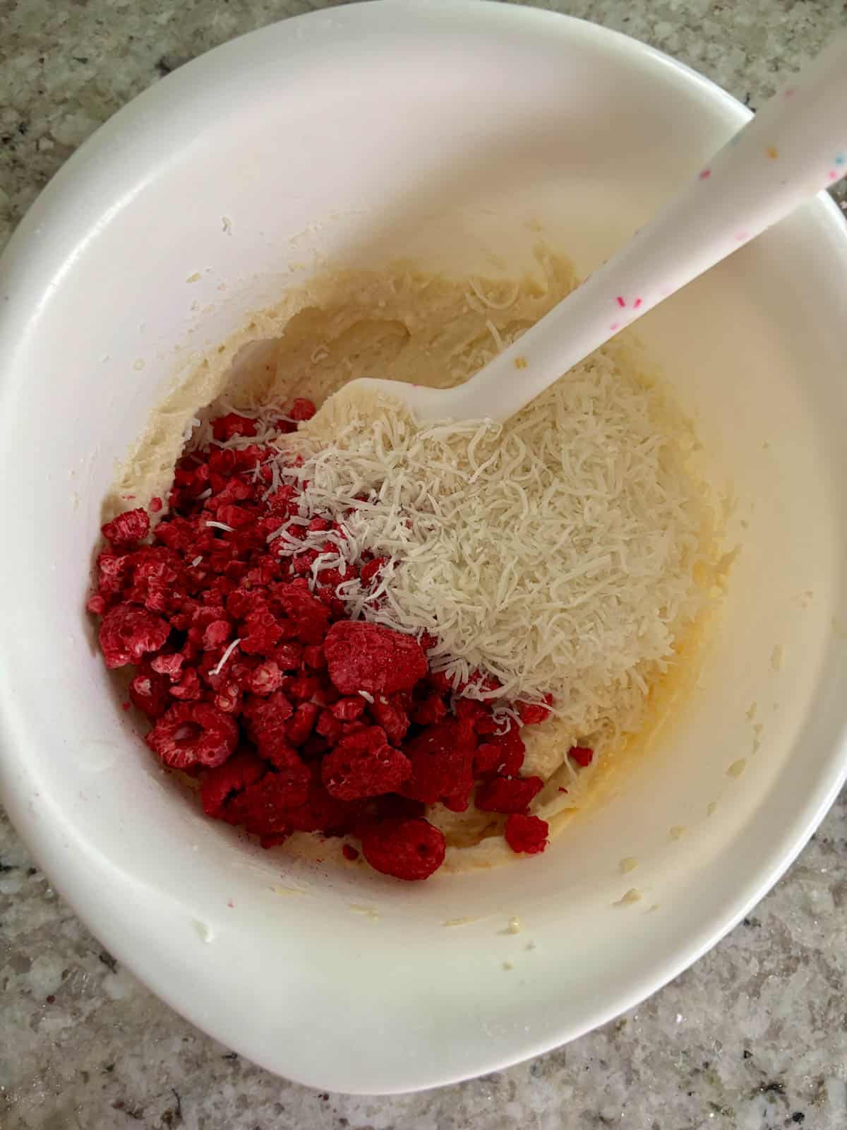 Shredded coconut and fresh raspberries being added to the coconut cake batter.