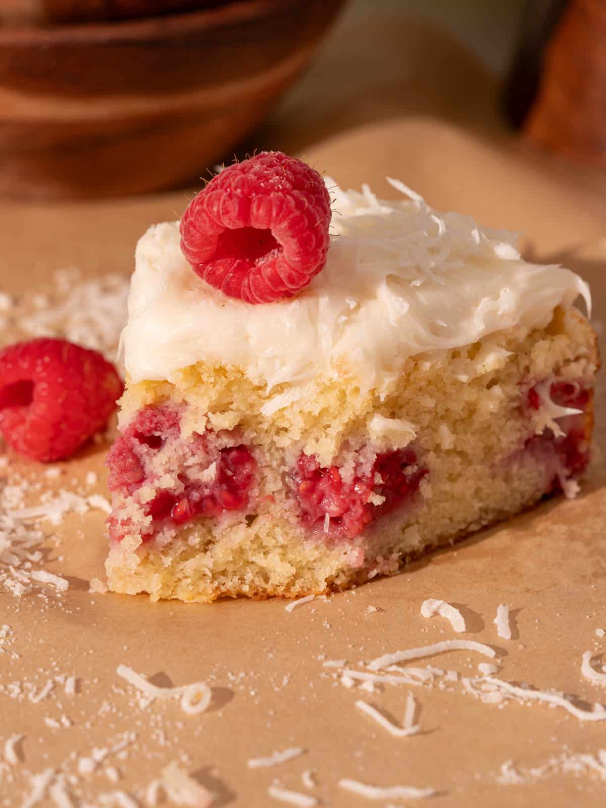 Showing the cake with a bite taken out showing the fresh raspberries and cream cheese frosting.