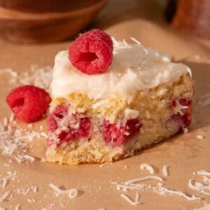 Coconut raspberry cake with cream cheese frosting on top and fresh raspberry and coconut.