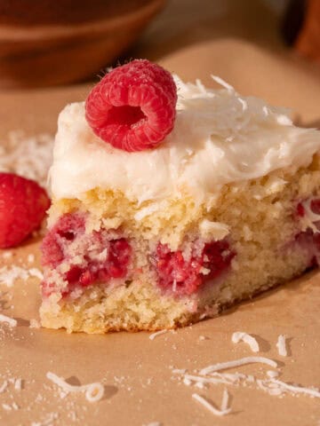 Coconut raspberry cake with cream cheese frosting on top and fresh raspberry and coconut.