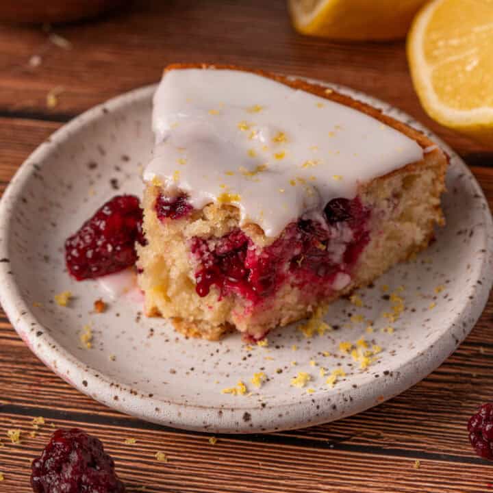 Lemon blackberry cake slice on a white plate with blackberries around and lemon zest.