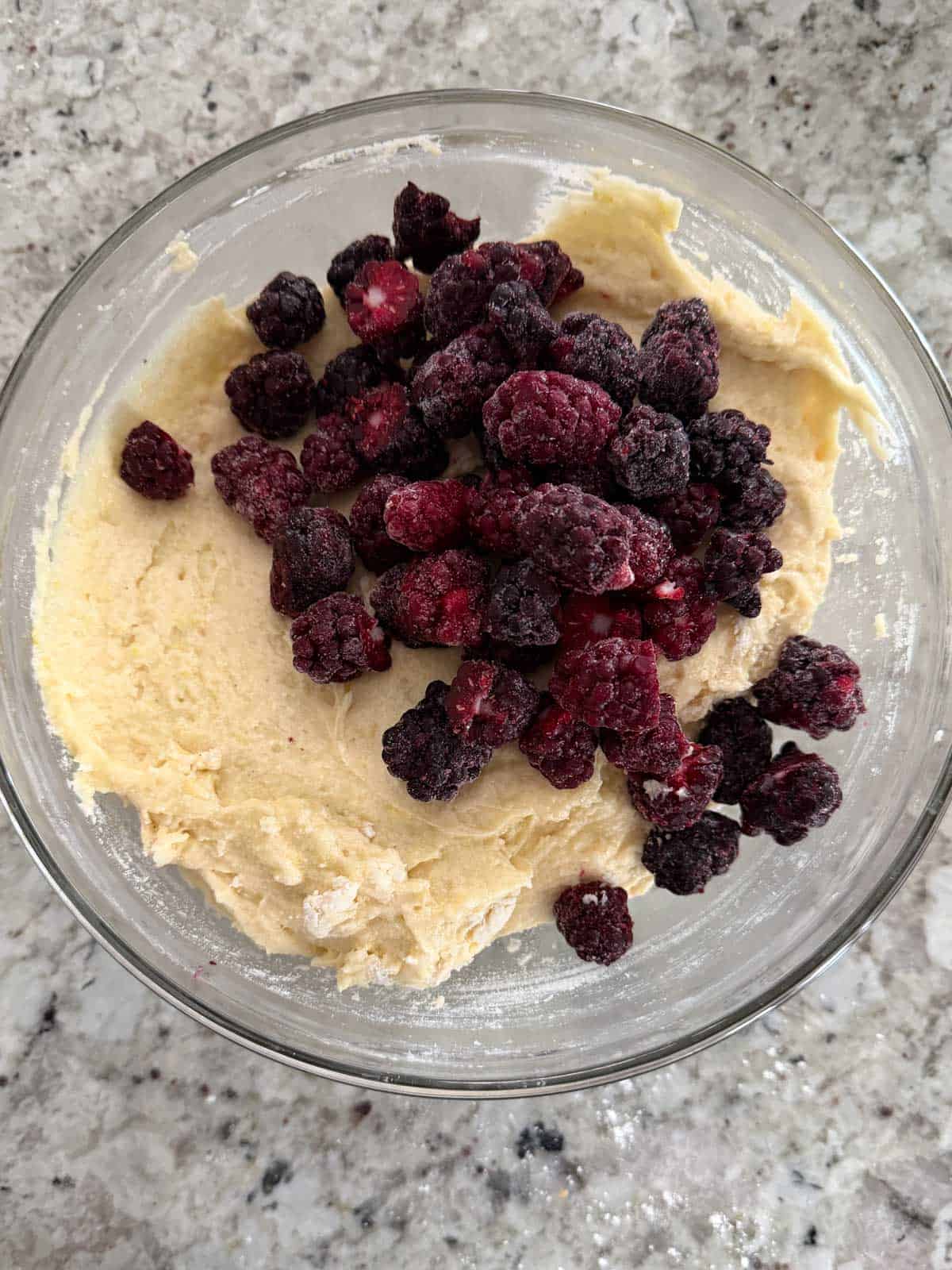 Blackberries being added to the lemon cake batter in a glass bowl.