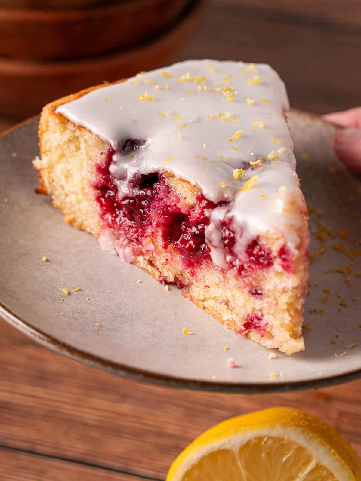 A slice of the blackberry and lemon cake on a plate with lemon zest on top.