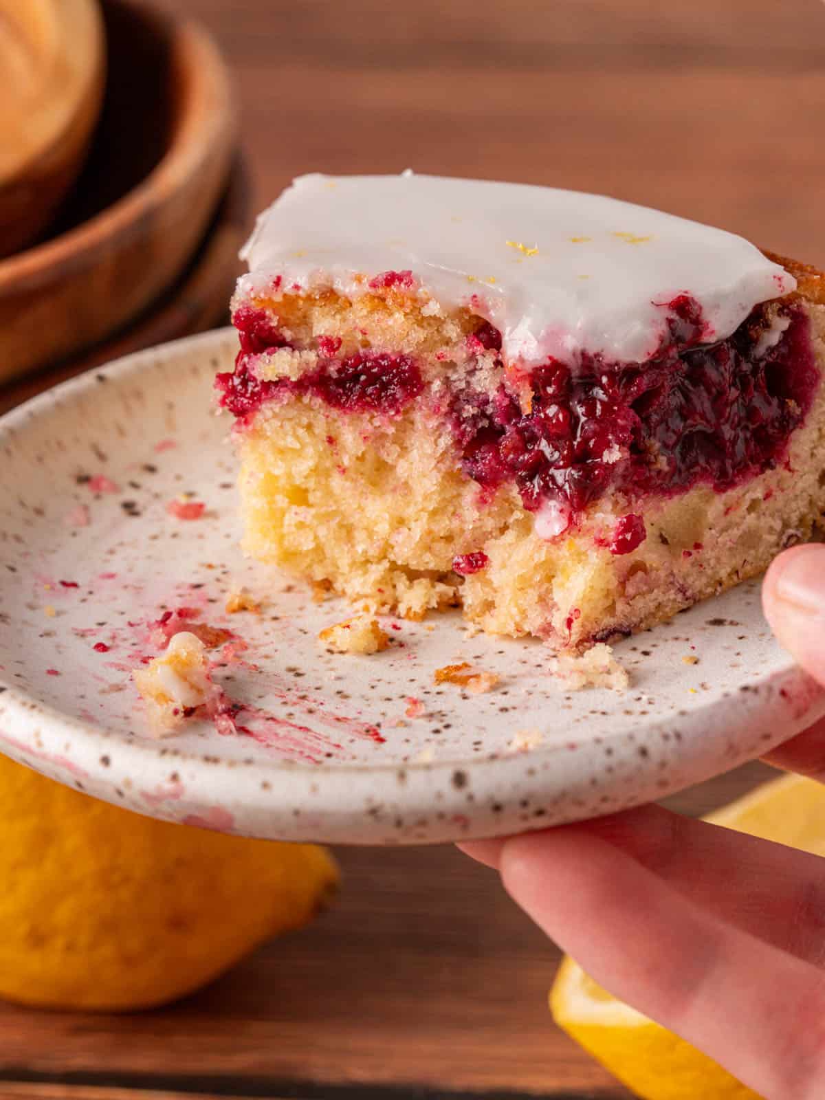 A piece of cake on a white plate with lemons in the background and bowls.