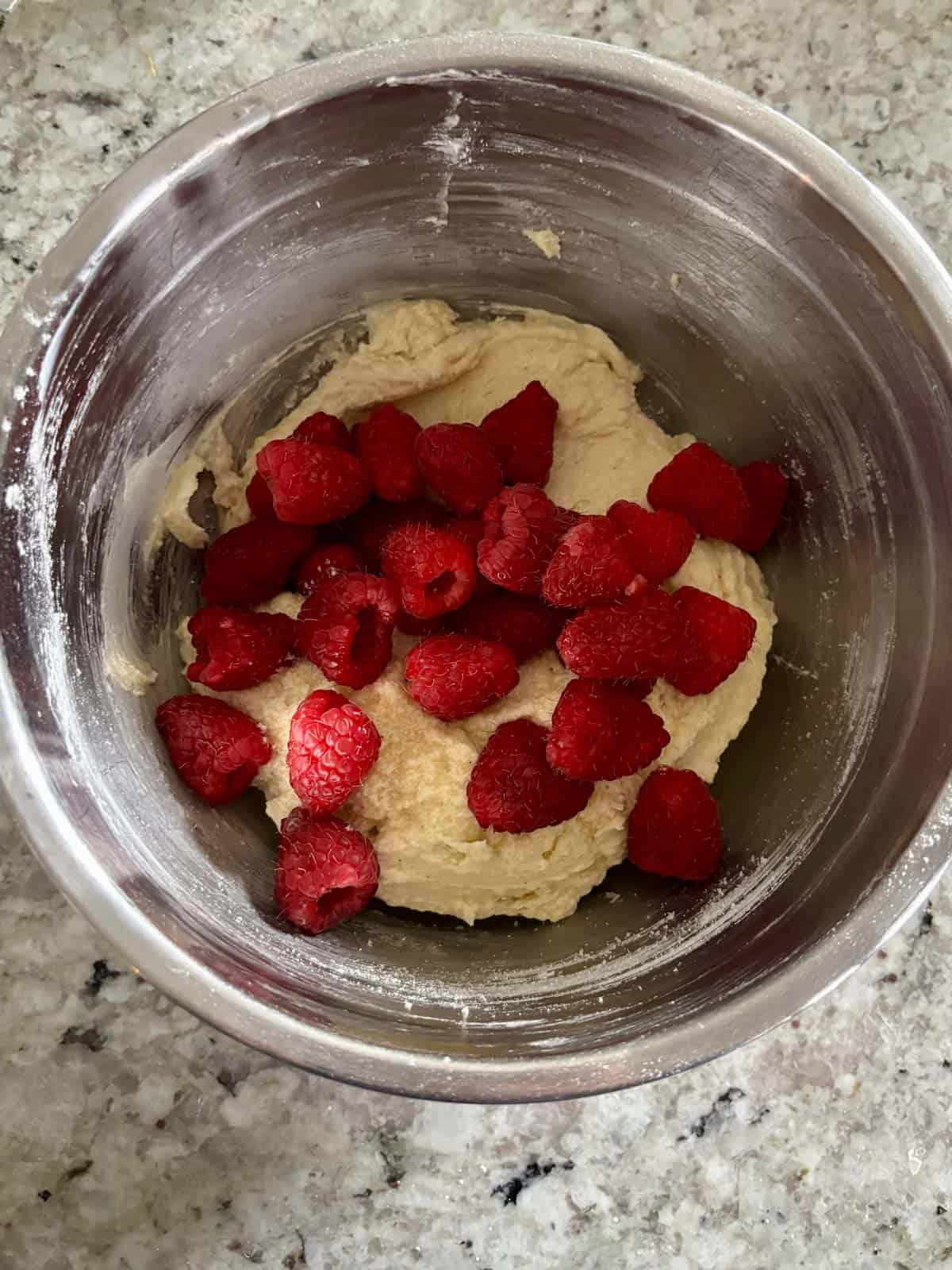 Fresh raspberries being added to the almond cake batter in a bowl.