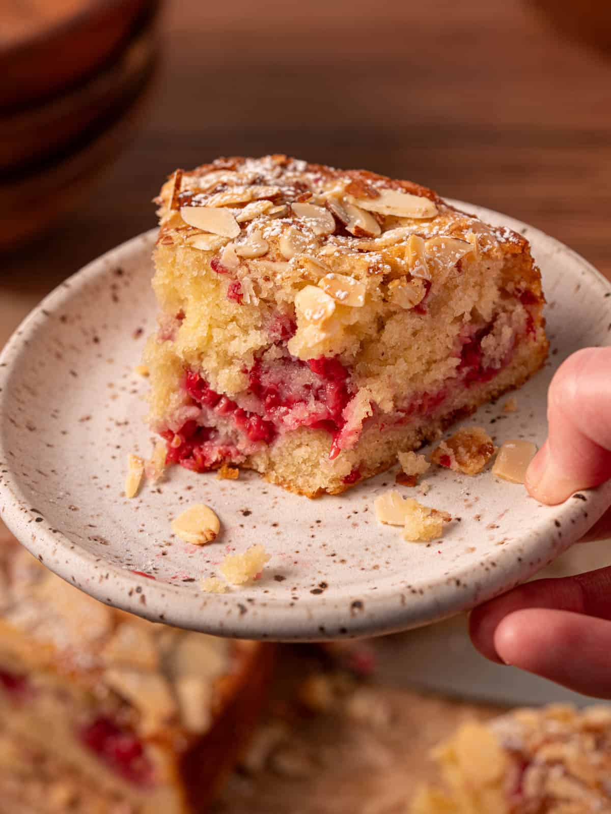 Almond raspberry cake on a plate with a bite taken out and almonds around it.