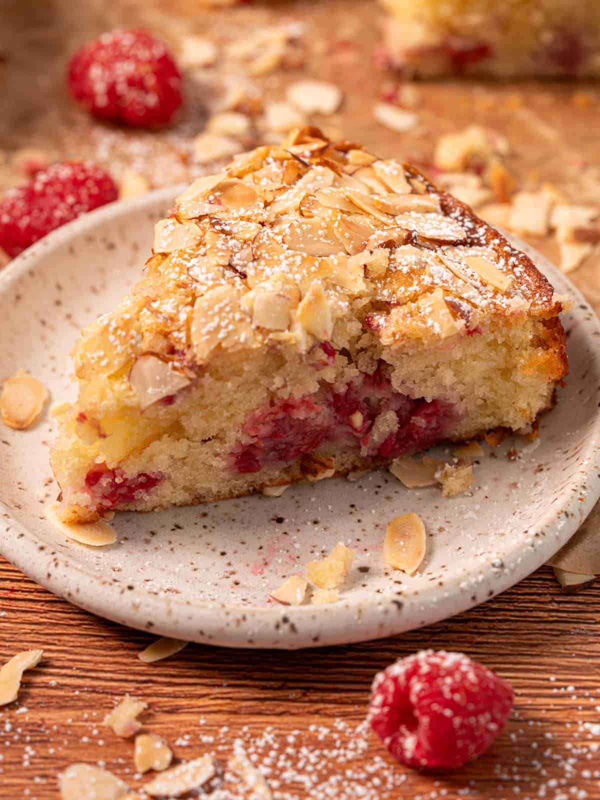 Raspberry almond cake slice on a plate with flaked almonds on top.