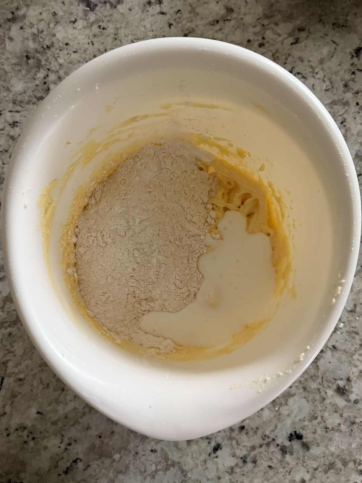 The dry ingredients and buttermilk being added to the butter egg mixture in a bowl.