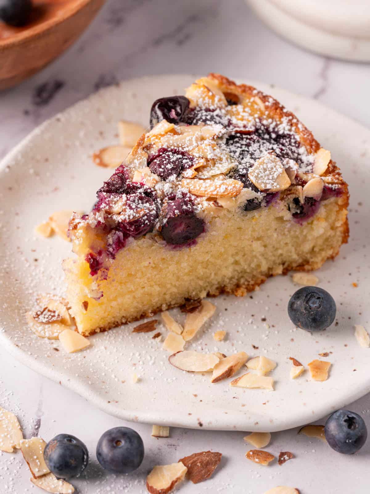 Lemon blueberry almond cake on a plate with blueberries and almonds around.