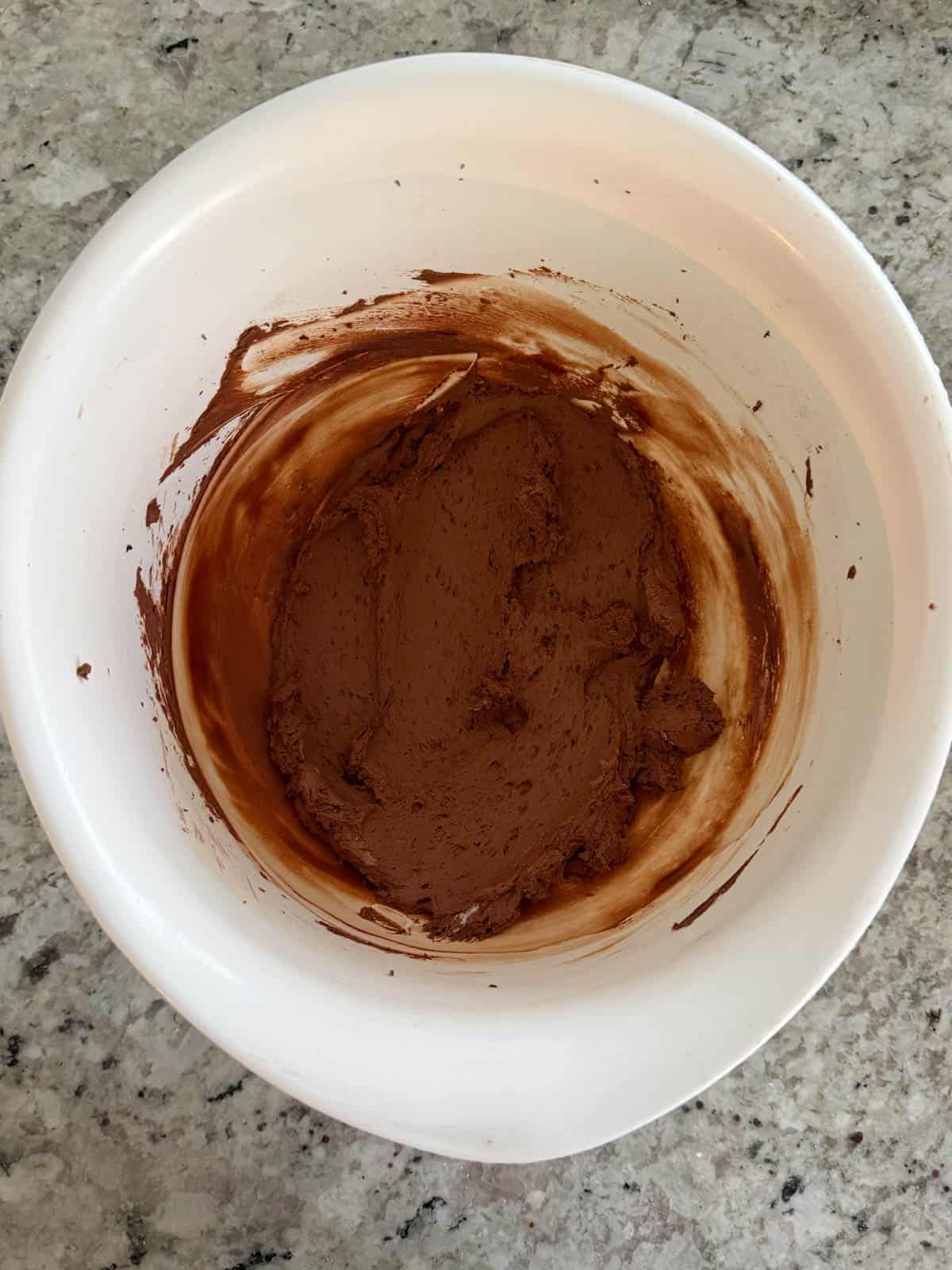 Sour cream being added to the butter and cocoa powder in a bowl.