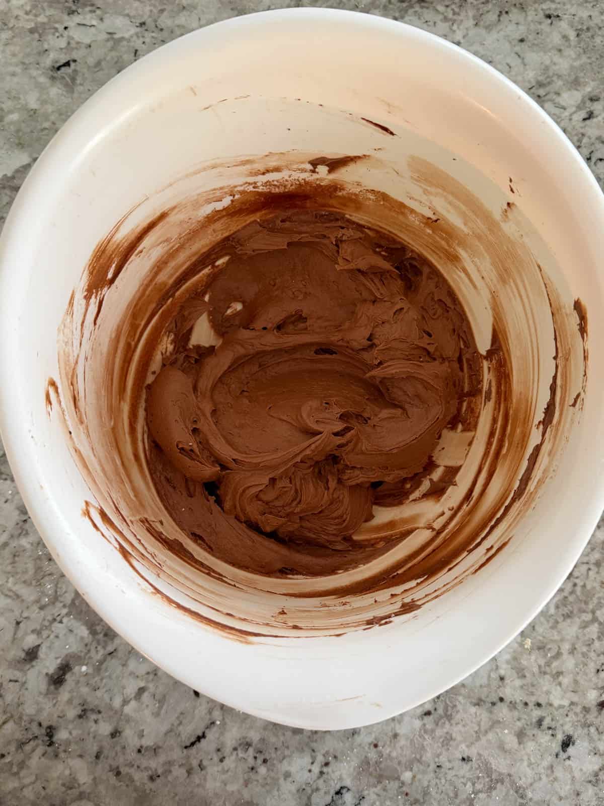 Powdered sugar being added to the butter cocoa sour cream mixture in a bowl mixed until smooth.
