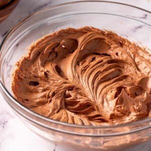 Chocolate sour cream frosting in a glass bowl on the counter.