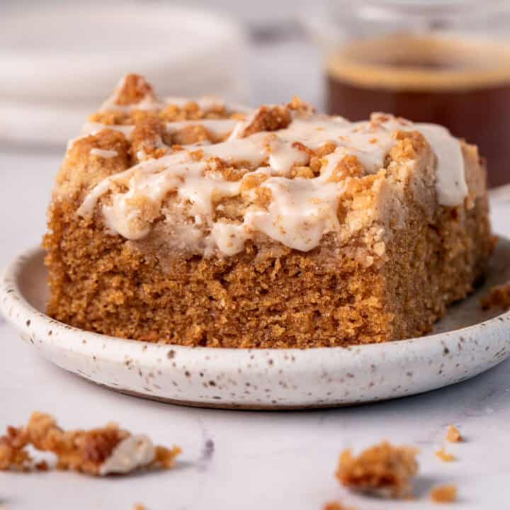 Actual coffee coffee cake slice on a plate with espresso icing on top and crumbs around it.