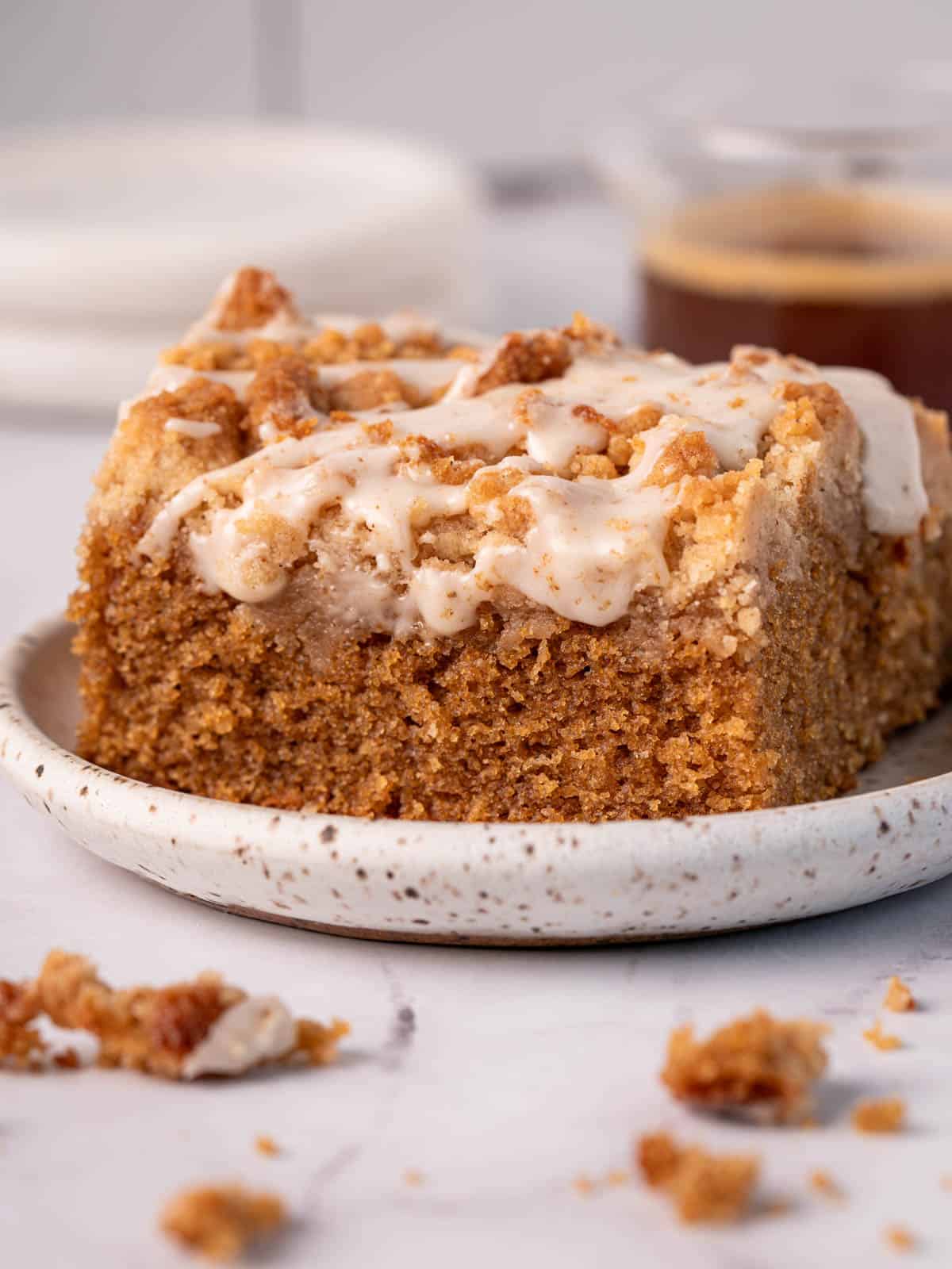 A slice of coffee cake with coffee icing on top on a white plate with crumbs around.
