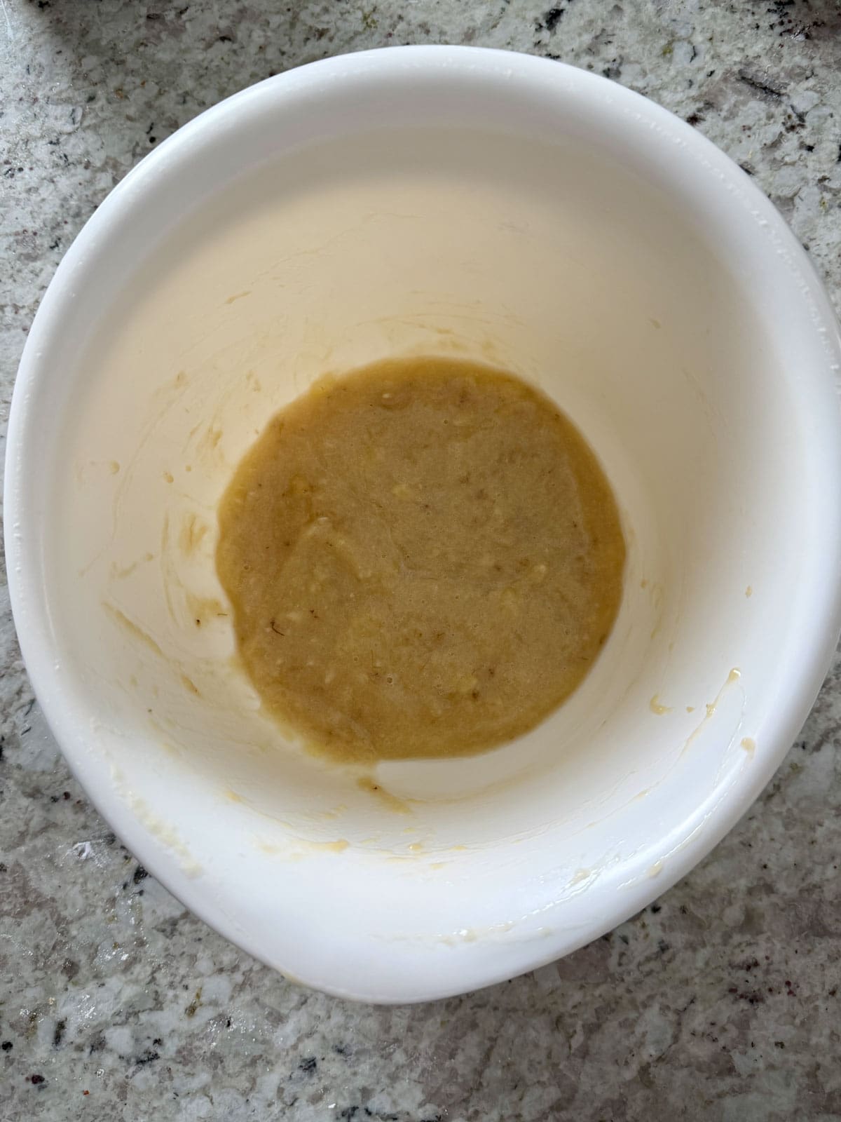 Mashed banana in a white mixing bowl on the counter.