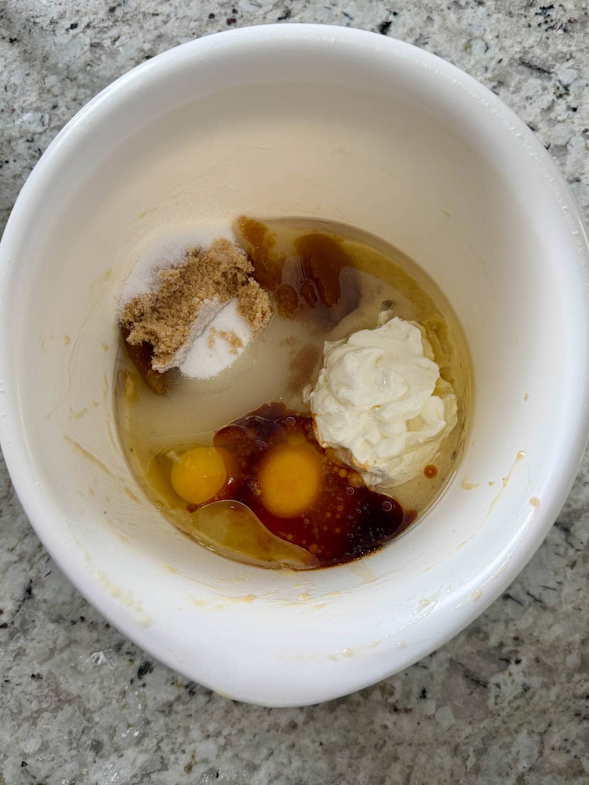 Brown and granulated sugar, eggs, oil, vanilla, sour cream, and banana in a mixing bowl.