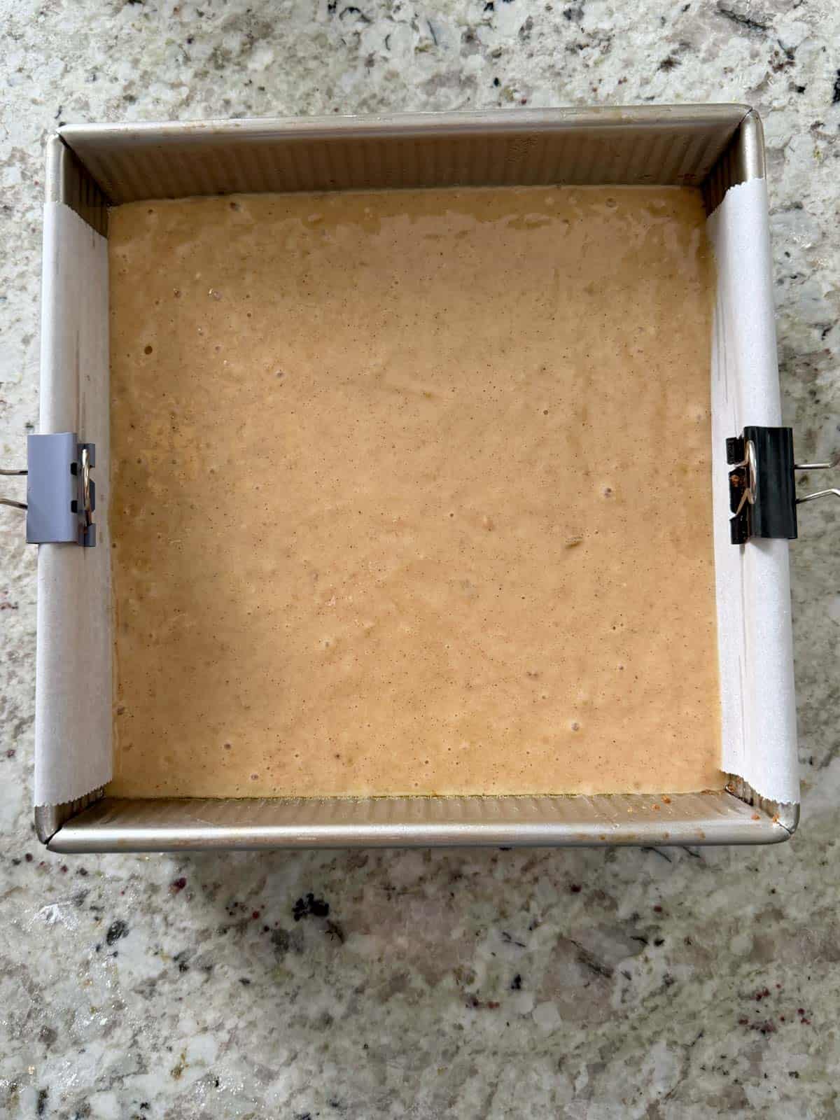 Spice banana cake batter in a 8X8 metal baking pan with parchment paper.