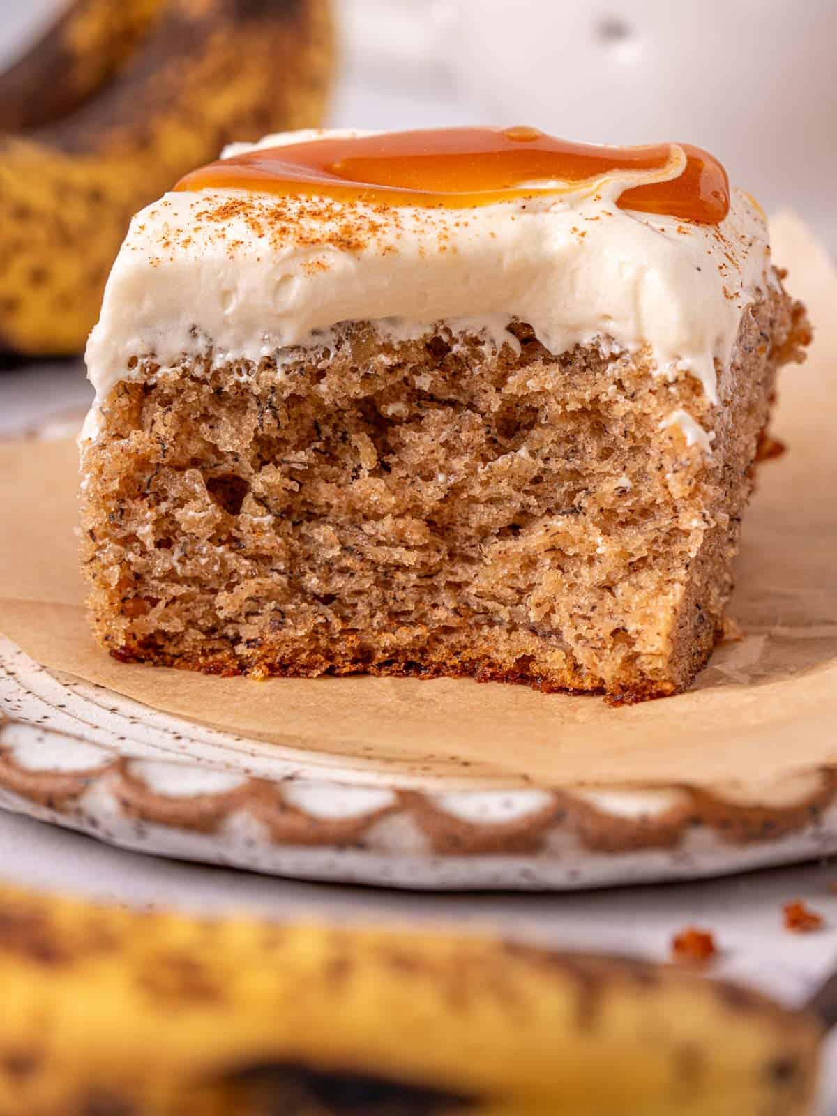 A slice of banana spice caramel cake on a plate with salted caramel on top and cinnamon.