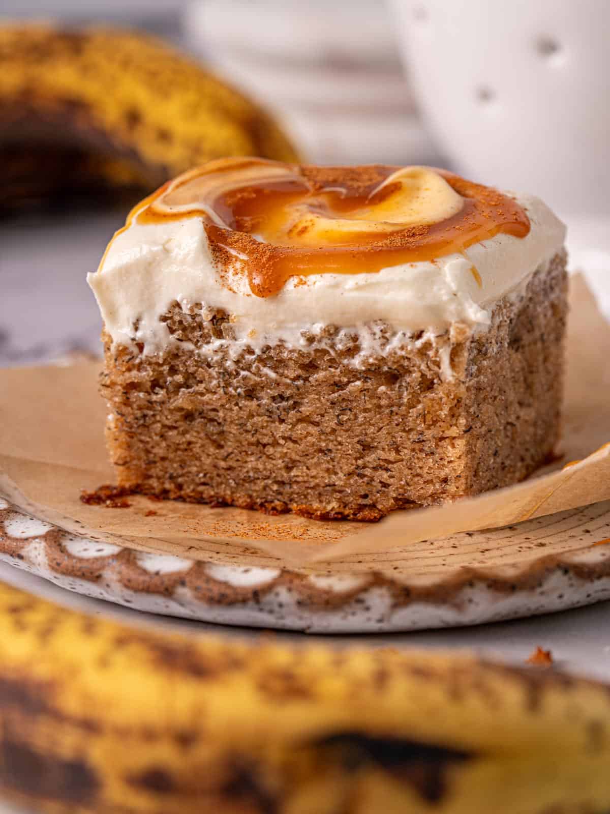 Old fashioned banana cake slice on a white plate with a swirl of caramel on top.