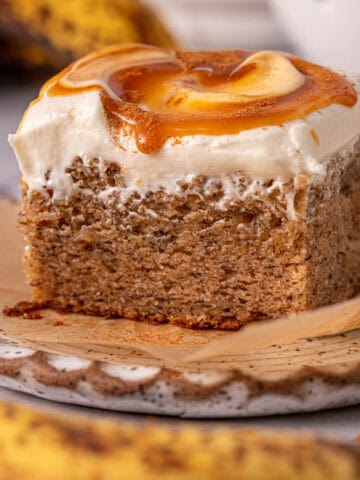 A slice of the best spiced banana cake on a plate with cream cheese frosting.