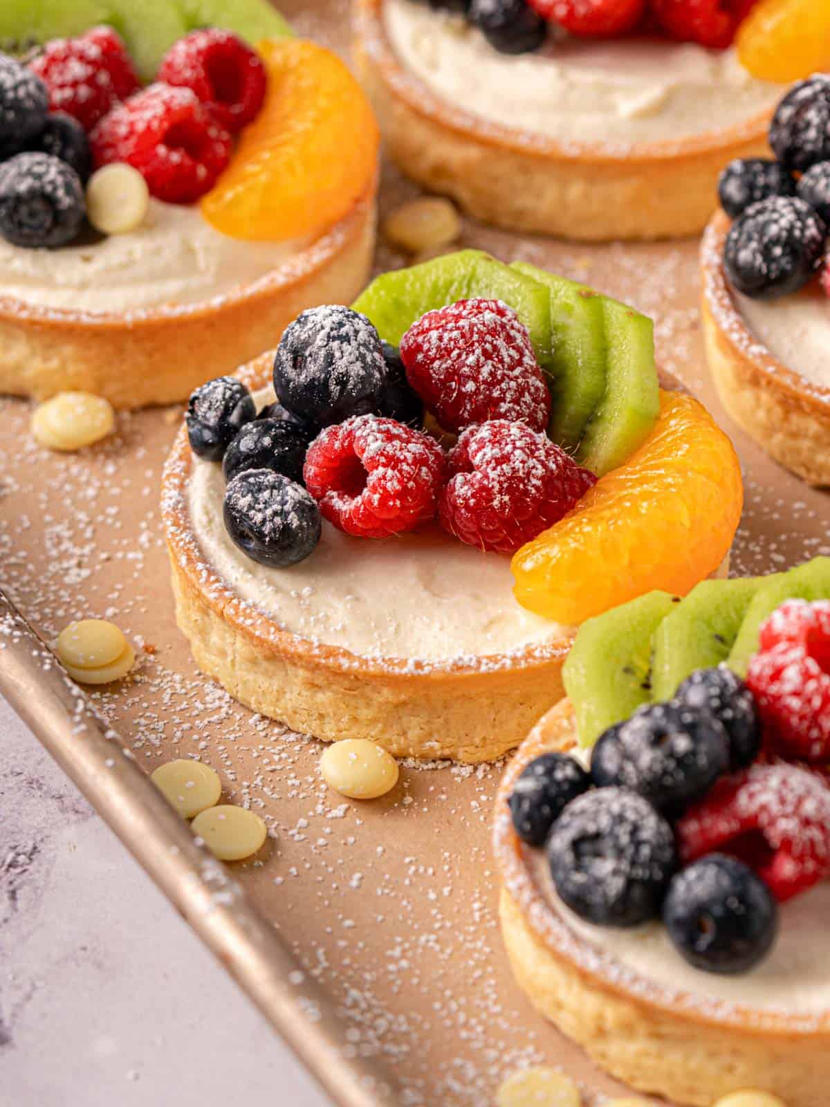 The tarts lined up on a baking sheet with white chocolate and fresh fruit.