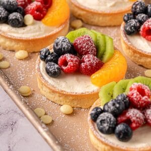 White chocolate tarts with fresh raspberries on top and white chocolate scattered around.