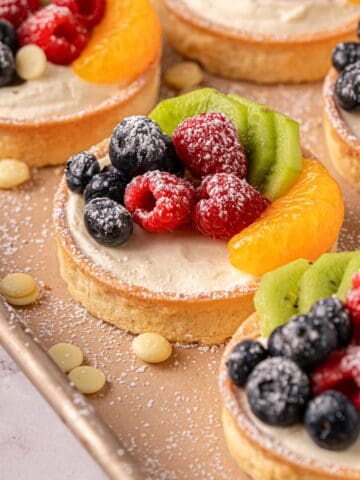 White chocolate tarts with fresh raspberries on top and white chocolate scattered around.