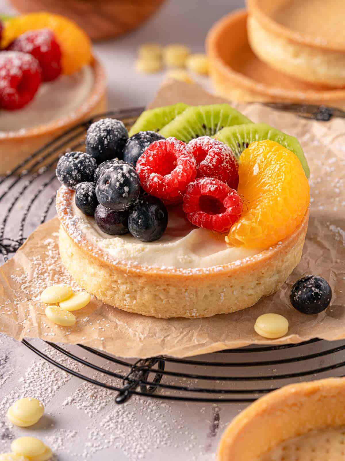 Raspberry white chocolate tarts on a cooling rack with powdered sugar and tart shells.