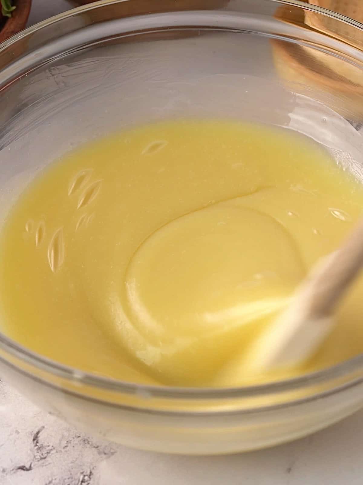 White chocolate ganache in a glass bowl on the counter being mixed together.