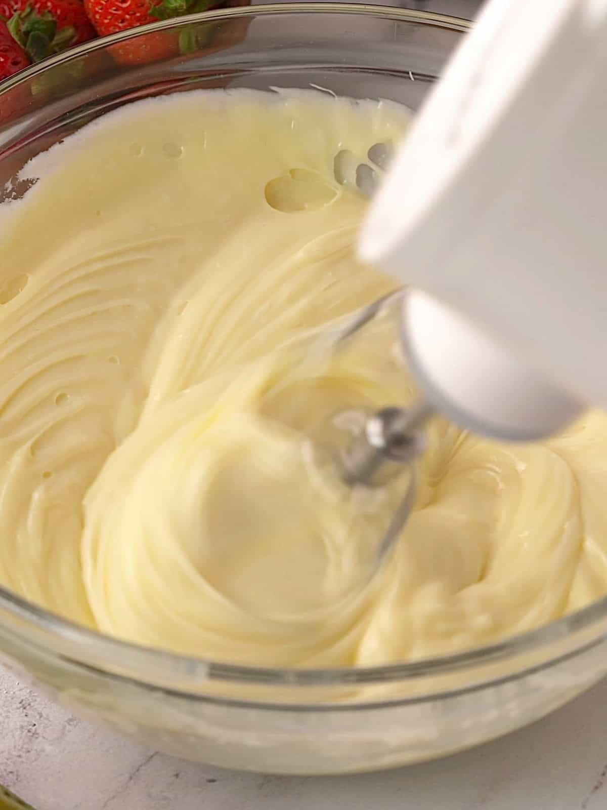 White chocolate ganache and cream cheese being mixed together in a bowl until combined.
