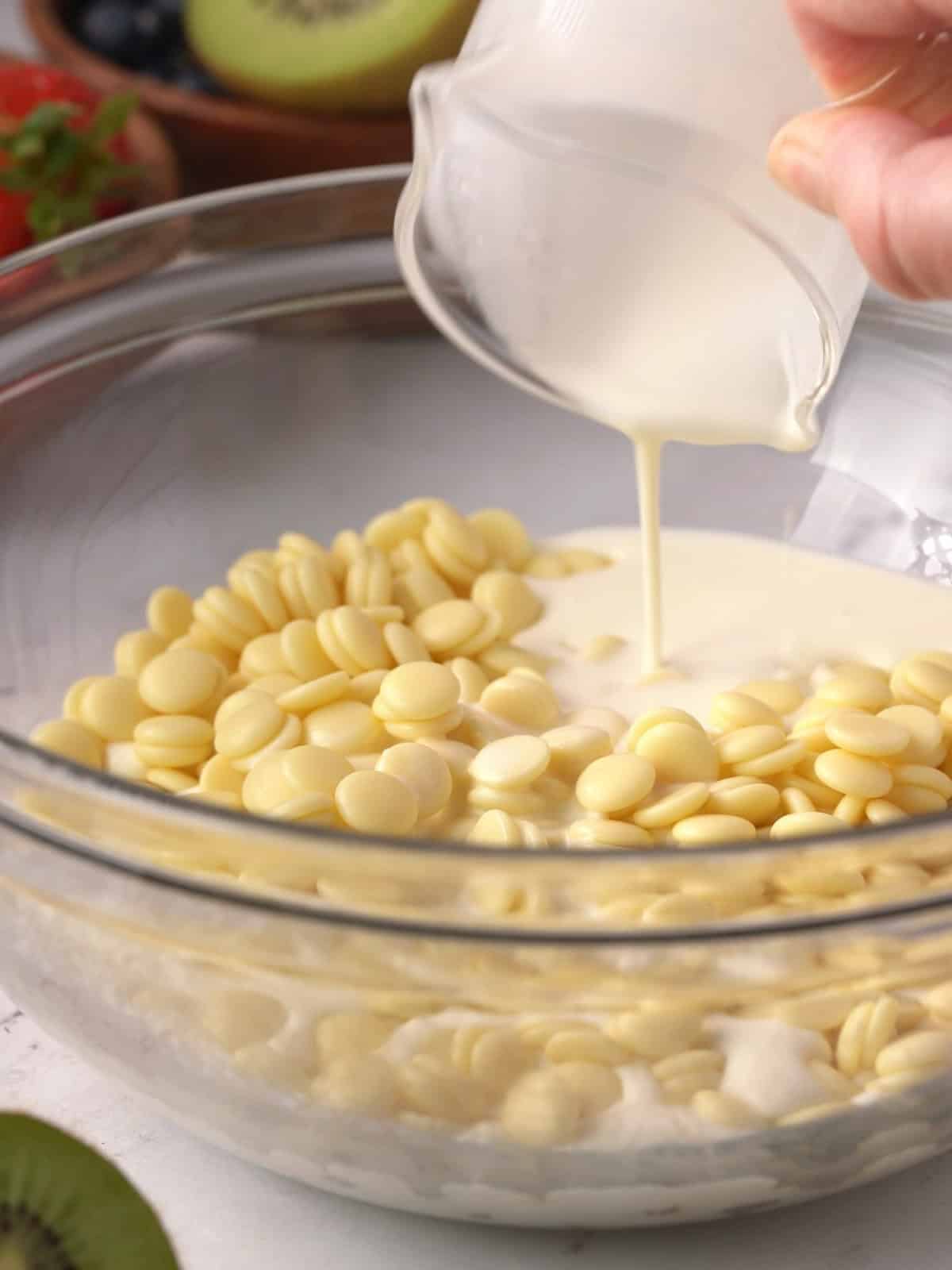 Adding heavy cream to the white chocolate in a bowl on the counter.