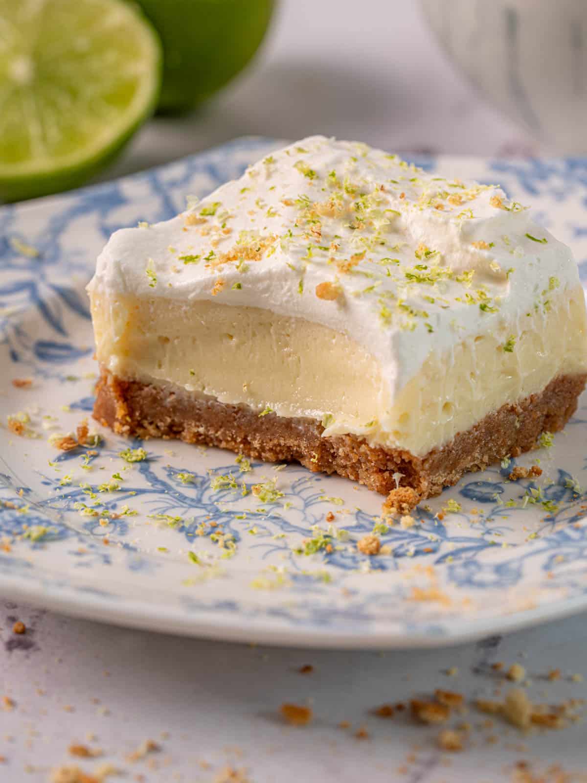 Creamy lime cheesecake bar with a gingersnap crust and lime zest on top on a plate.
