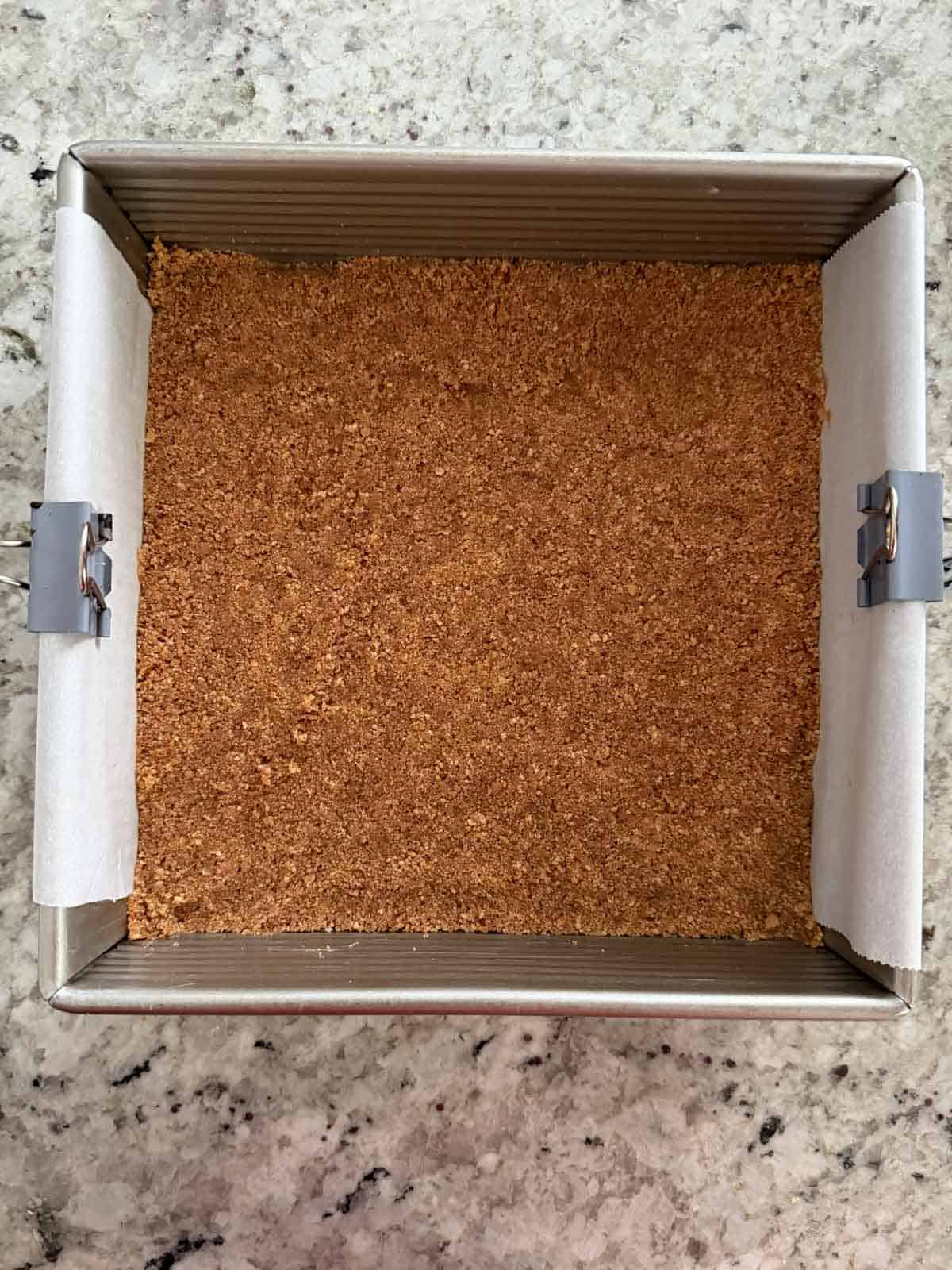 Graham cracker crust pressed down into a baking pan before being baked.