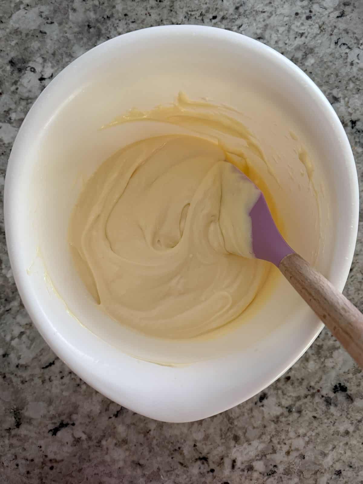 The smooth cheesecake batter in a bowl with a spatula in the counter.