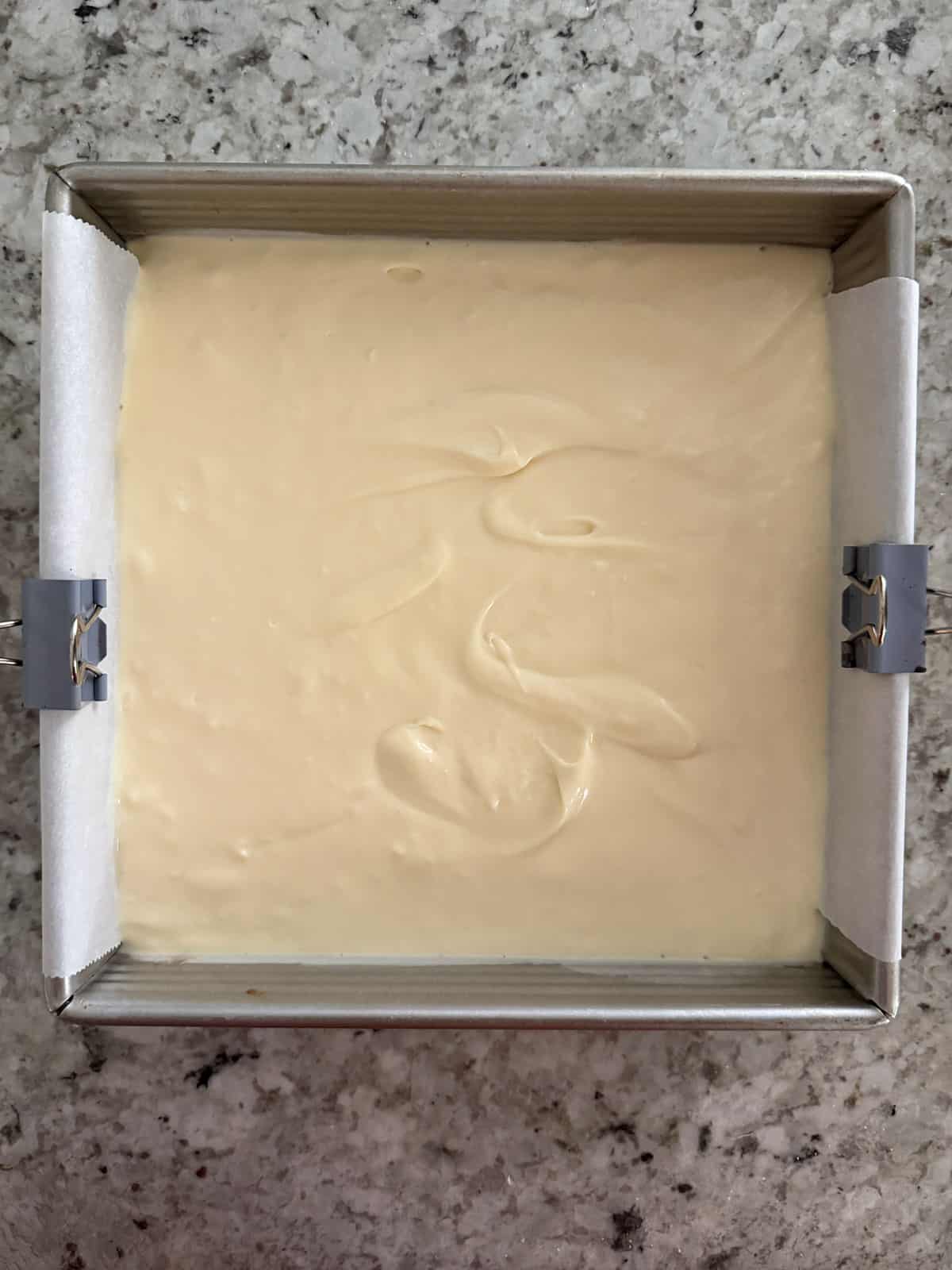 The cheesecake batter in a metal pan with parchment paper on the bottom.