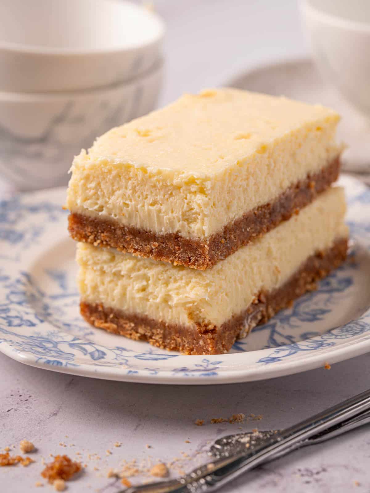 Baked cheesecake bars on top of each other on a blue plate with silverware.