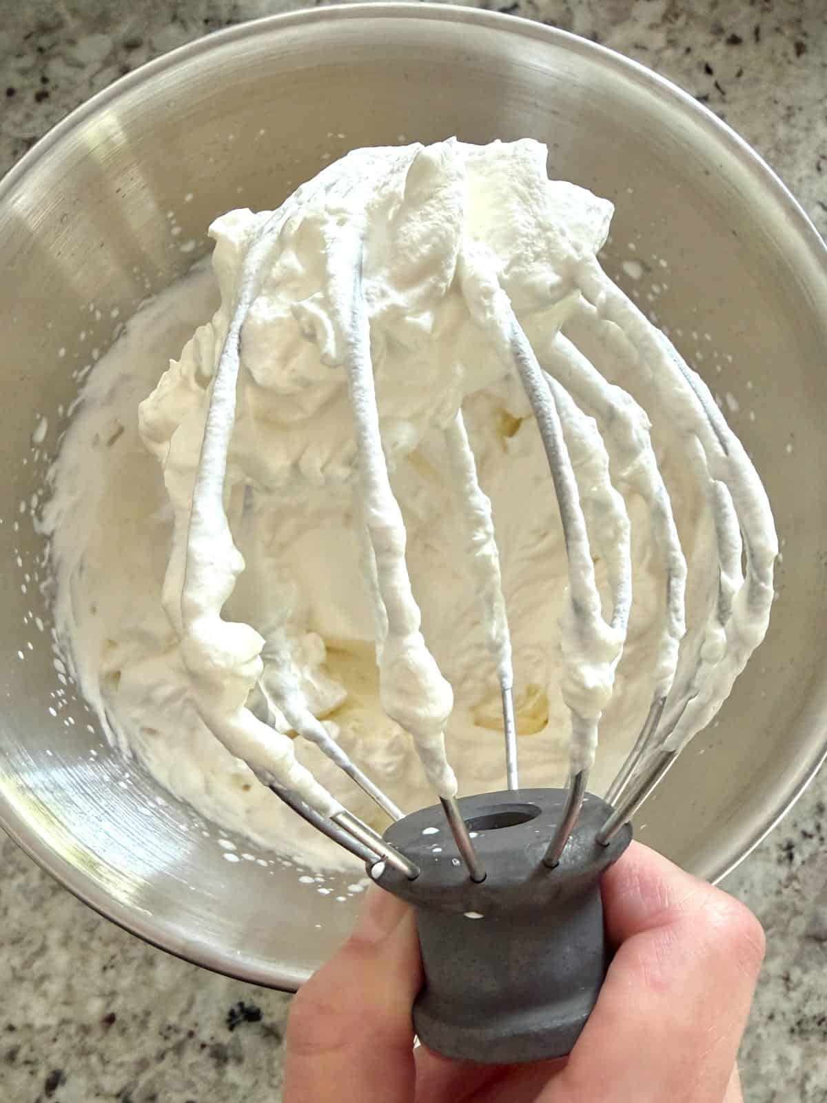 Heavy cream whipped until stiff peaks showing the peaks on a the whisk attachment.