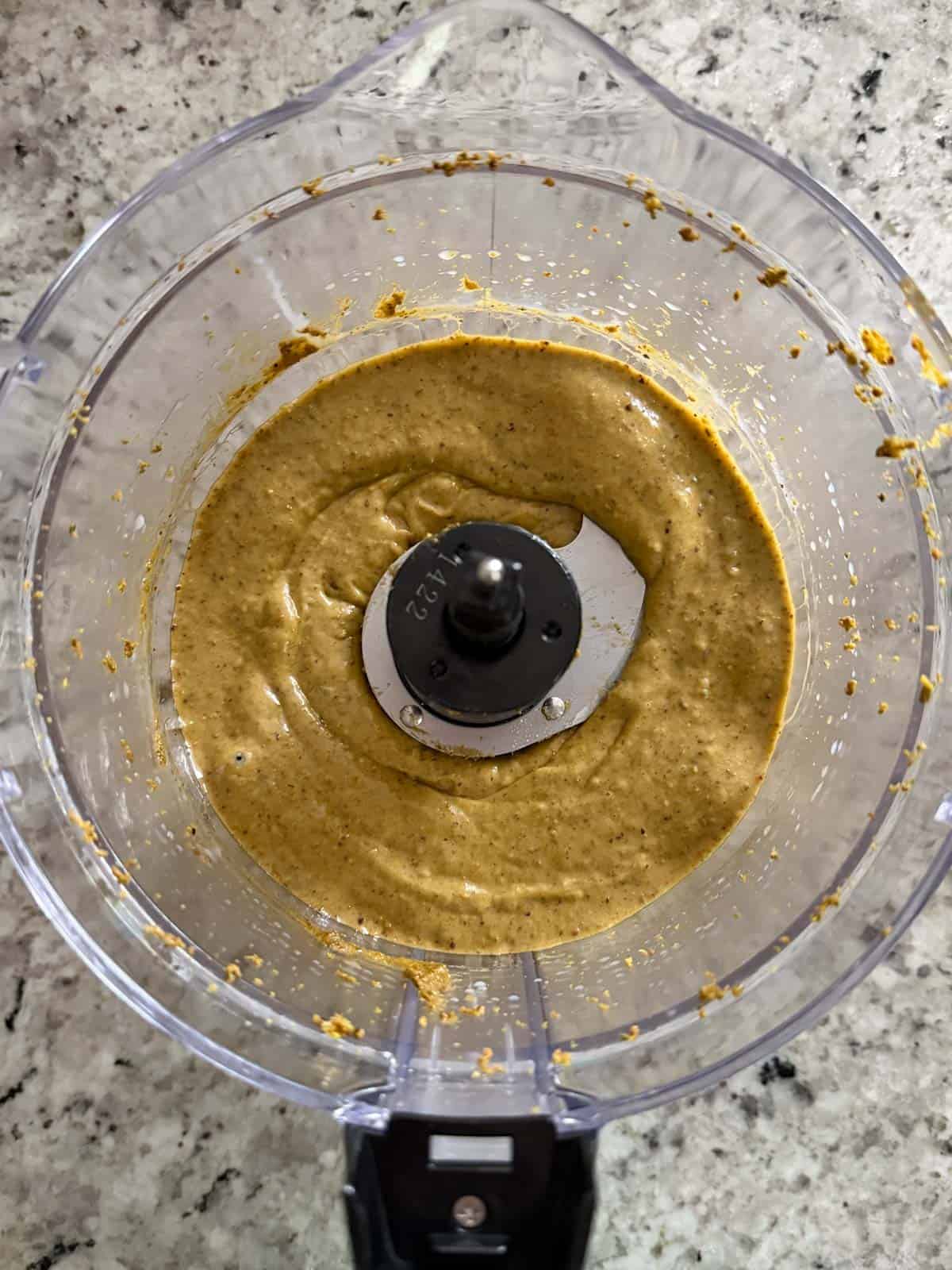 Sweetened condensed milk being added to the pistachio nut butter in a food processor.