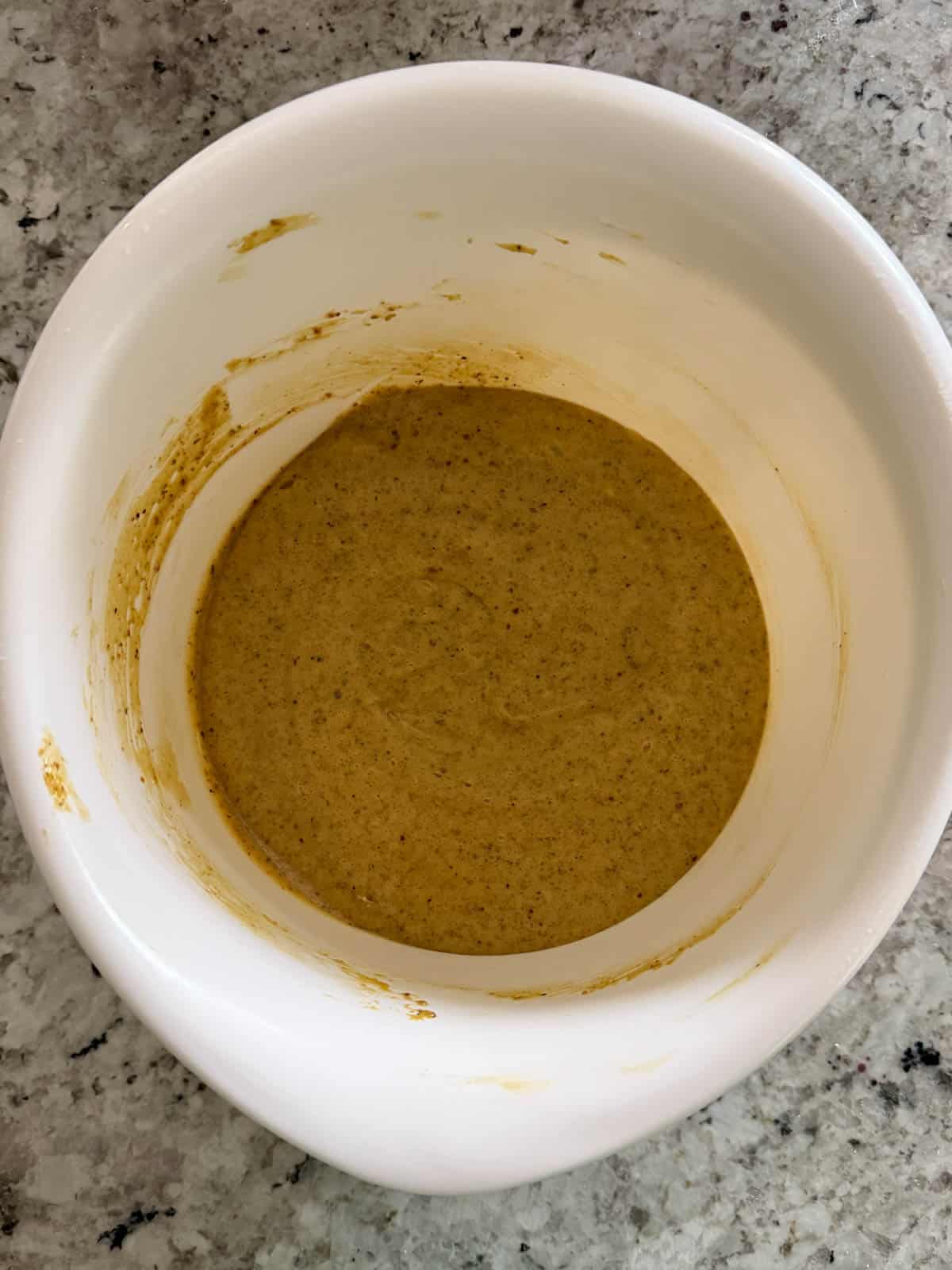 Cream cheese being added to the pistachio mixture in a white bowl on the counter.