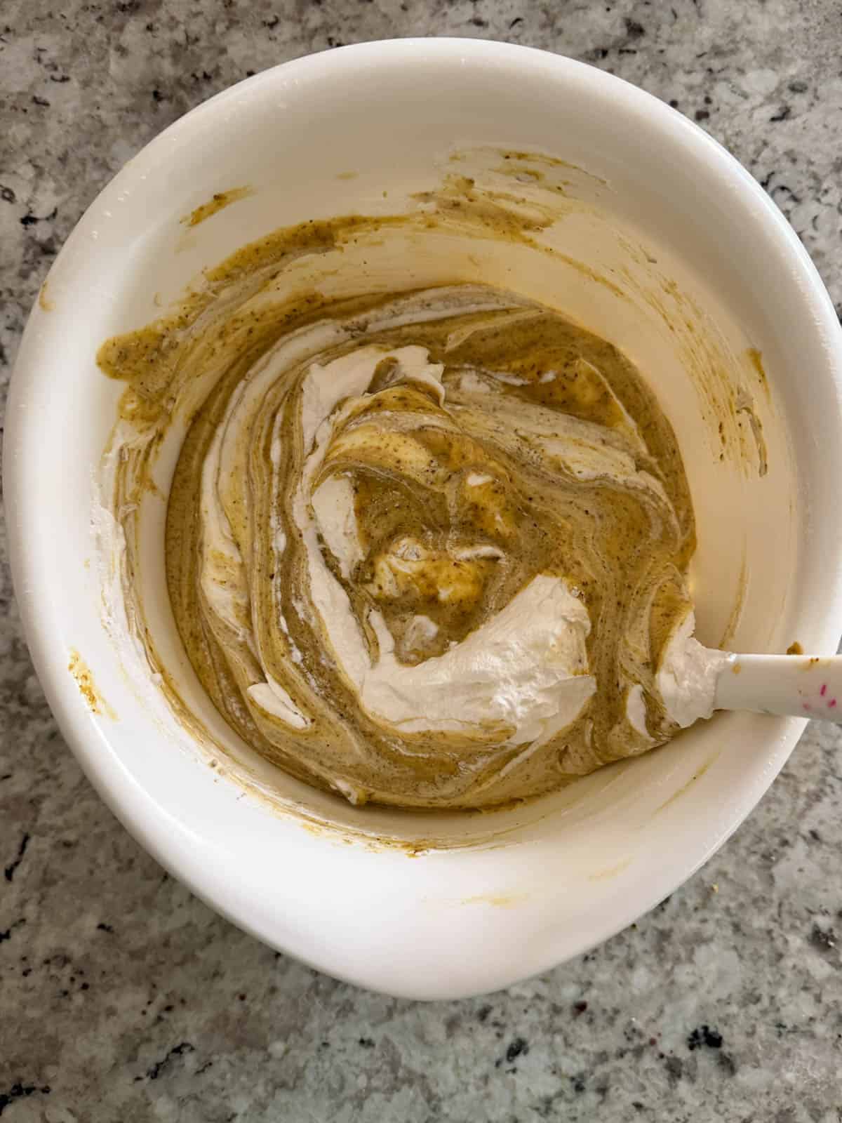 Folding whipped cream into the pistachio base in a white bowl.