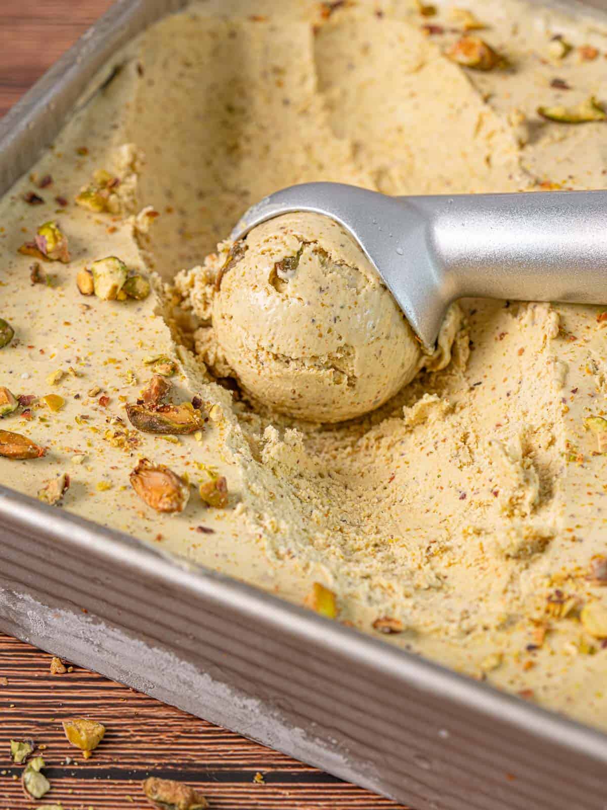 An ice cream scoop scooping out the best pistachio ice cream in a metal container.