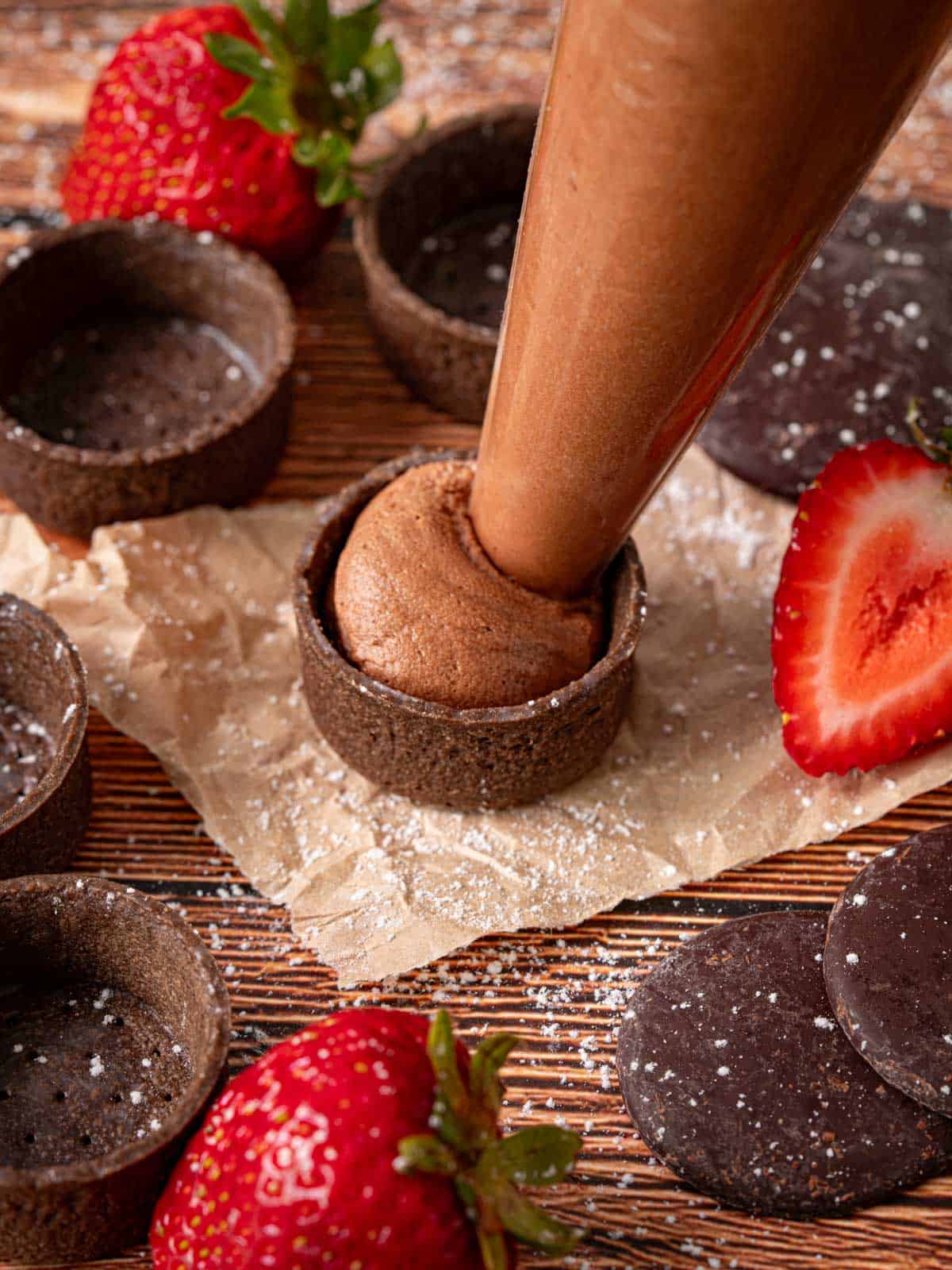 Filling the tart shells on the counter with strawberries around it.