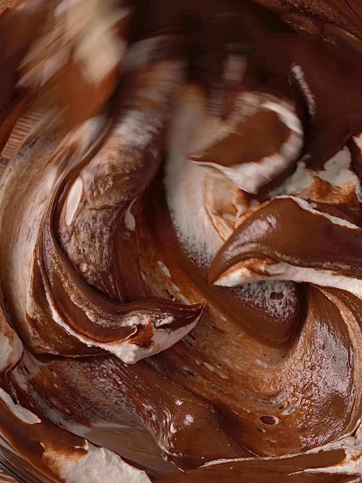 Folding the whipped cream into the chocolate mascarpone mixture in a bowl.
