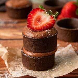 Chocolate strawberry tartlets stacked on top of each other with fresh strawberries.