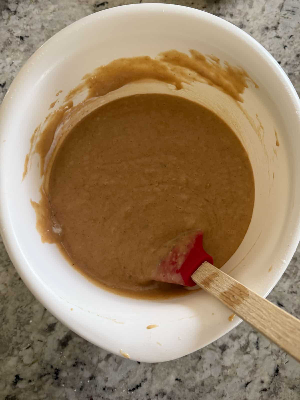 Banana bread batter in a white bowl with a spatula on the counter.