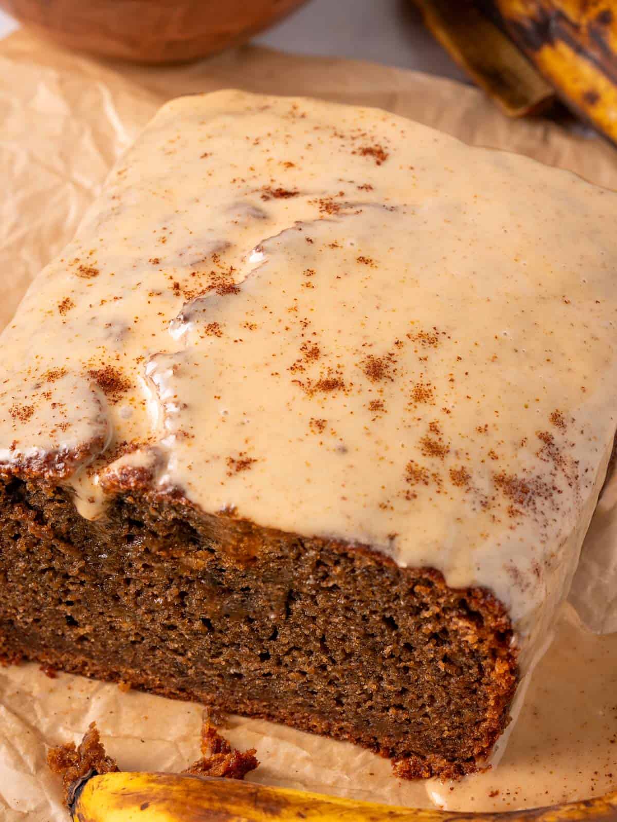 Coffee glaze on top of the banana bread with bananas around it and parchment paper.