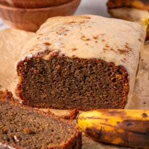 Coffee banana bread loaf with glaze on top with overripe bananas in the background.