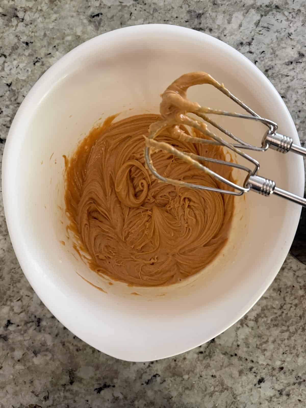 Peanut butter, sweetened condensed milk, vanilla, and salt in a white bowl on the counter.